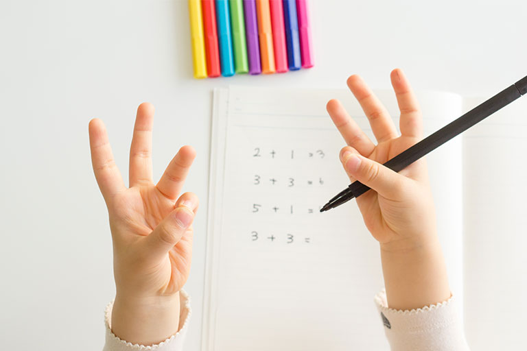 child counting on fingers as they fill out a math worksheet