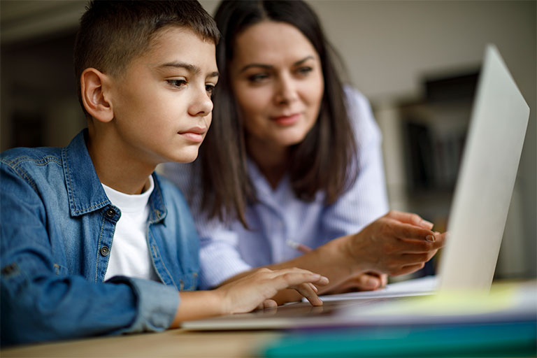 Adult helping student on laptop