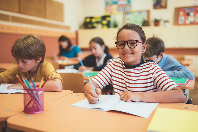 Girl looking up from her desk work in a classroom of kids.