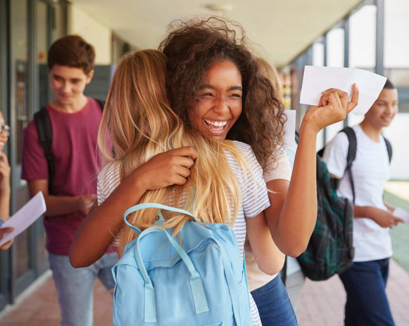 2 students hugging and smiling with report card in hand.